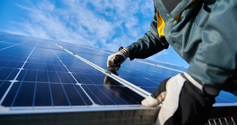 Gloved installer fitting a rigid solar panel under a blue sky