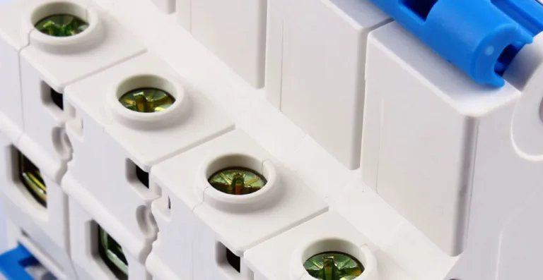 Close-up of a row of white miniature circuit breakers, showing the cable terminal screws and a blue switch