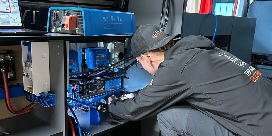 Tiny Build Electrics electrician wiring a solar charge controller and busbars inside a cabinet