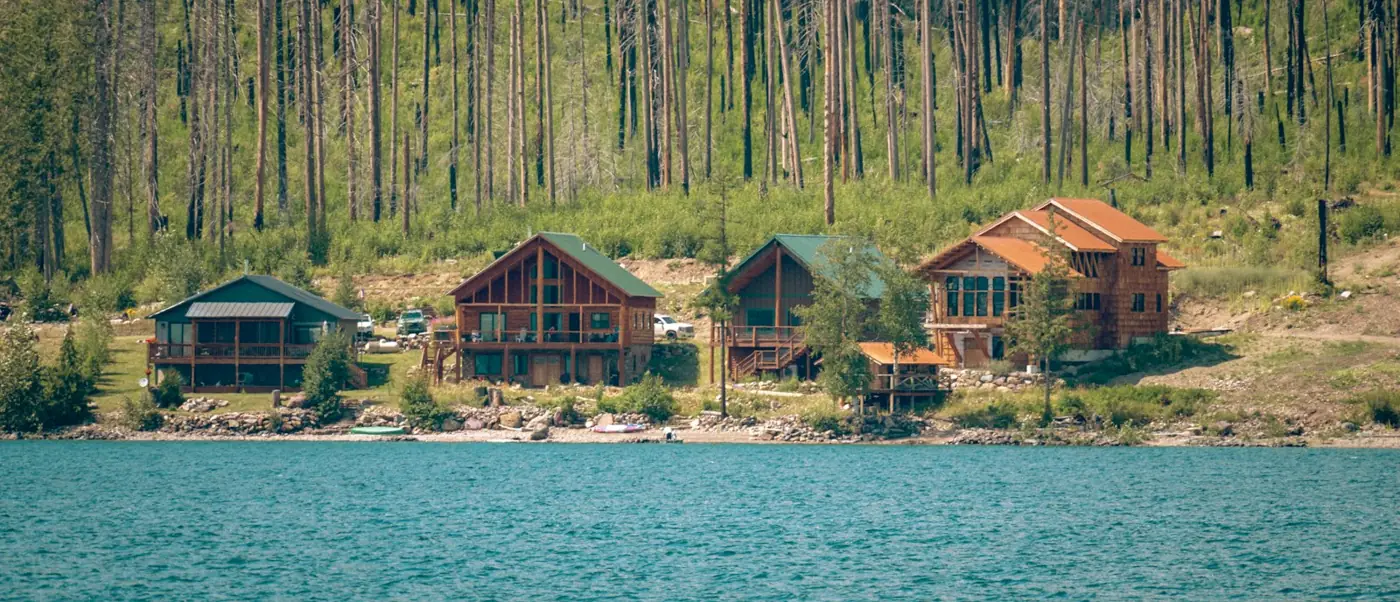 Row of timber holiday lodges along a lake shore below a wooded hillside