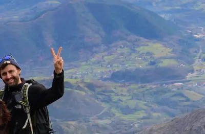 Smiling hiker giving a peace sign on a mountain ridge above a green valley
