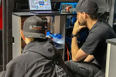 Two Tiny Build Electrics team members going through a wiring diagram on a laptop in the workshop