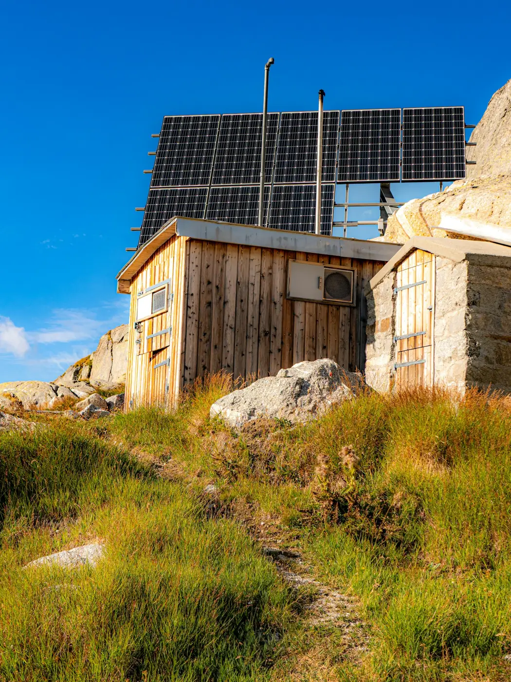 Remote timber hut on a rocky hillside with a bank of solar panels mounted above the roof